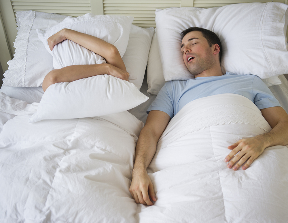 Snurkende man in bed en vrouw onder kussen tegen geluid