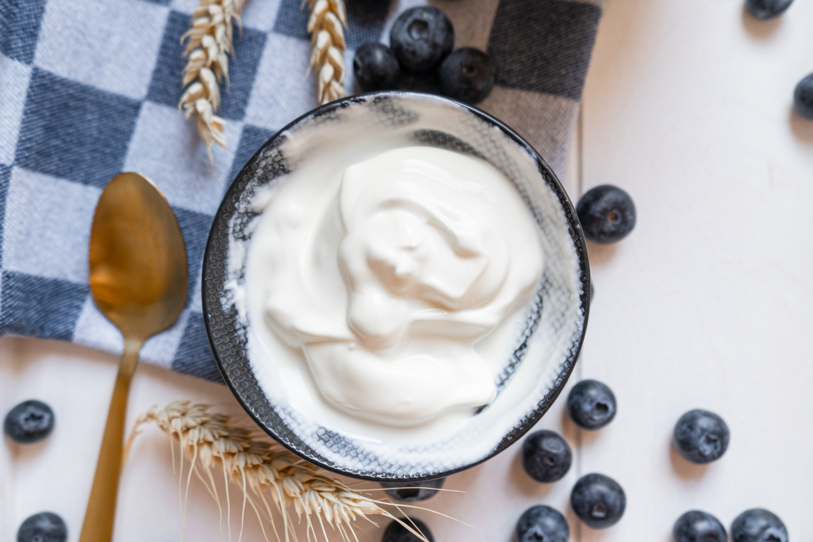 Yoghurt in een kom op een tafel met blauwe bessen en een blauw geruite theedoek