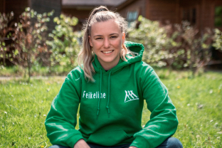 Feikeline Valkema zit op de grond in het gras met een groene trui aan