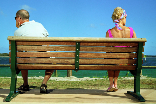 Man en vrouw zitten elk aan een kant van een bankje en kijken uit op zee