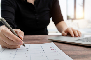 Vrouw zit achter laptop en schrijft iets in agenda