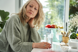 Vrouw die aan tafel zit met een glas water met nadenkende blik