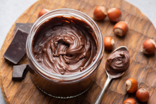 Hazelnootpasta in een potje met daarnaast hazelnoten en chocoladestukjes